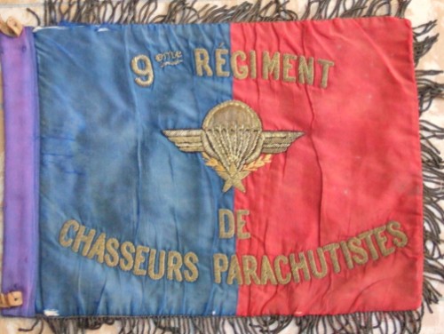 Le fond des deux faces est identique , bande verticale BLEU roi à la hampe et bandes verticales ROUGE aux parties flottantes .A l' avers l'inscription 9° RÉGIMENT de CHASSEURS PARACHUTISTES brodée en cannetille d'or encadre un Brevet de Parachutiste brodé or et argent